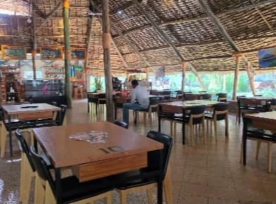 Wooden tables with built-in grills and black chairs in the open-sided dining hall