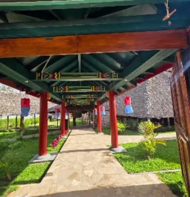 A covered walkway of red pillars and painted beams leading through the garden