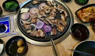 Meat, onion and garlic cooking on a round table grill, surrounded by side dishes