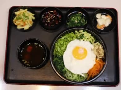 A tray with bibimbap topped with a fried egg, soup and small side dishes