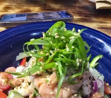 Ceviche salad of raw fish, tomato and onion piled with spring onion and sesame in a blue bowl